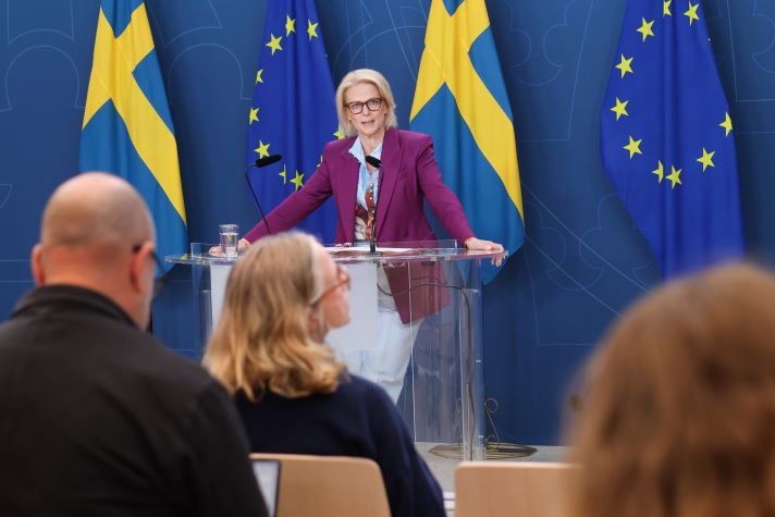 Elisabeth Svantesson, Minister for Finance, standing against a backdrop of Swedish and EU flags.