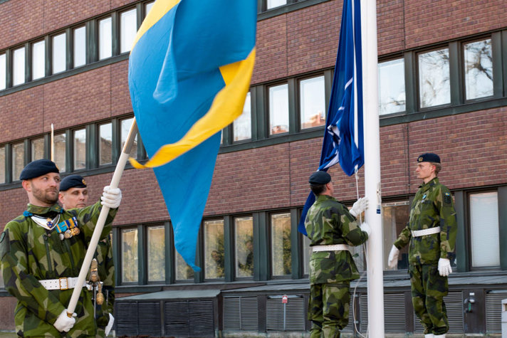 Soldiers raising a NATO flag and a Swedish flag.