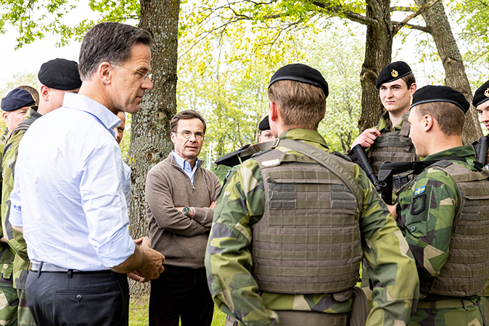 Ulf Kristersson and Mark Rutte talking to military men.