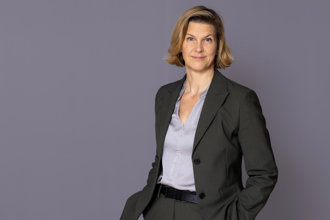Minister for Gender Equality Nina Larsson stands in front of a gray wall and looks into the camera.