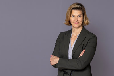 Minister for Gender Equality Nina Larsson stands in front of a gray wall and looks into the camera.