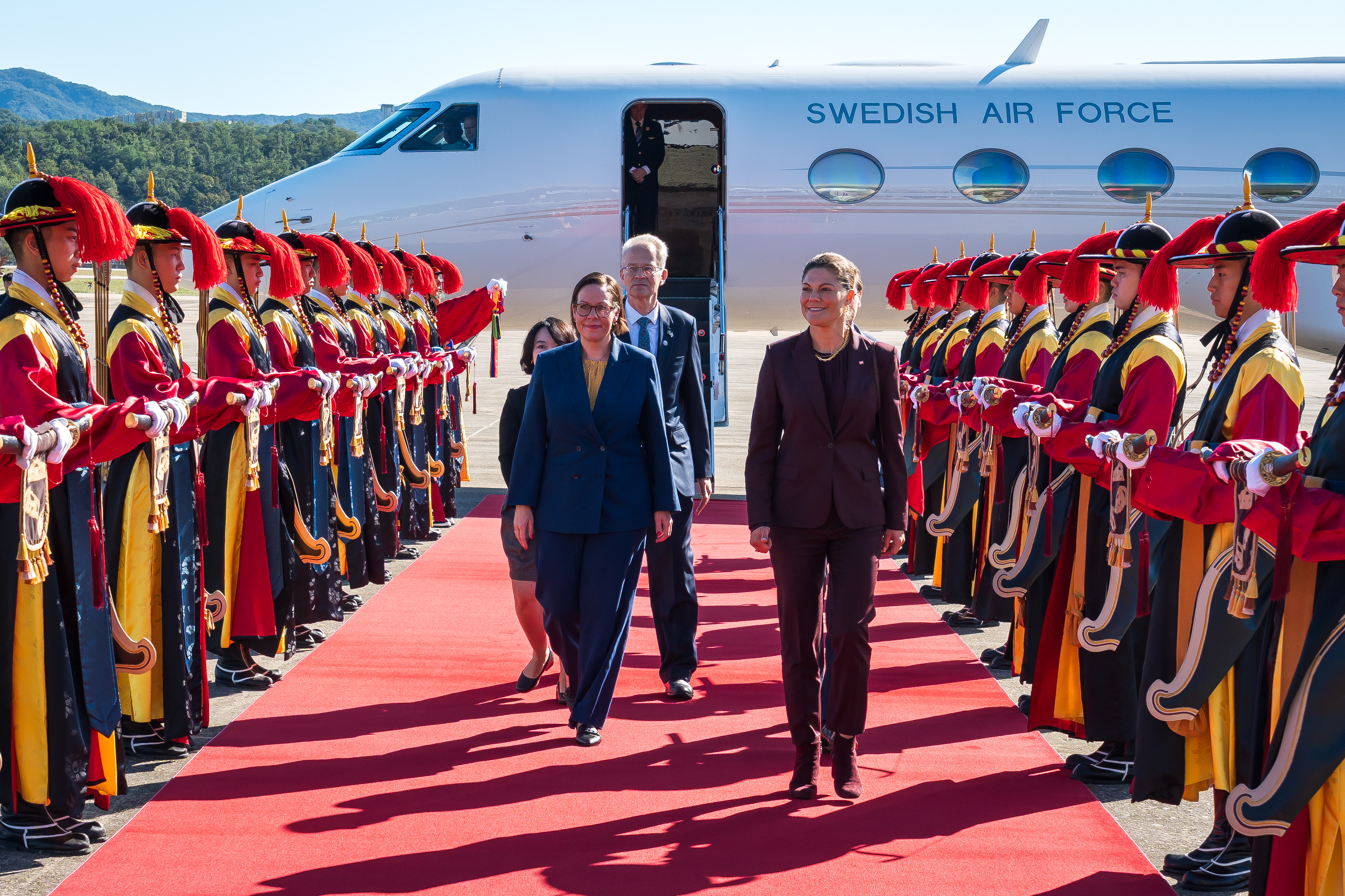 Crown Princess Victoria and Minister for Foreign Affairs Maria Malmer Stenergard walking down red carpet in front of airplane.