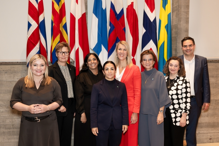 Women and men standing in front of the Nordic flags for a group photo.