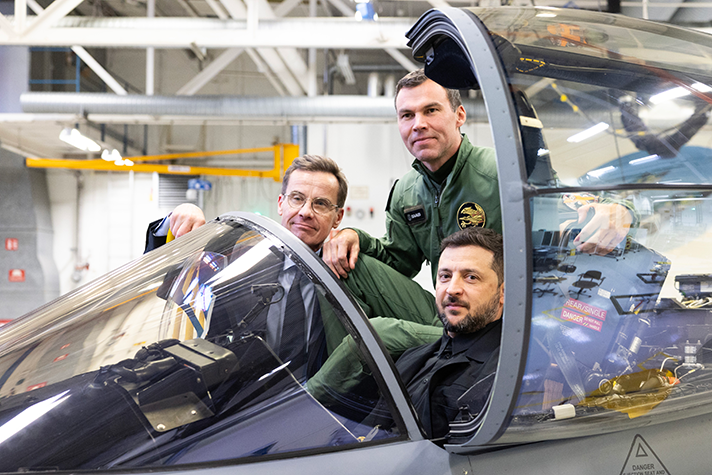 Ulf Kristersson, Volodymyr Zelenskyj and Marcus Wandt sitting in a JAS Gripen standing in a hangar.