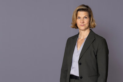Minister for Gender Equality Nina Larsson stands in front of a gray wall and looks into the camera.