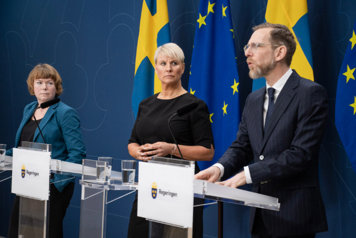 Minister for Older People and Social Security Anna Tenje, Minister for Social Affairs and Public Health Jakob Forssmed and Malin Danielsson, senior policy spokesperson for the Liberal Party stands in the Government's press room behind podiums. Behind them are Swedish flags and flags of the European Union.