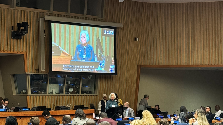 Minister Ankarberg Johansson delivers a speech. Her face is on a big screen in an auditorium.